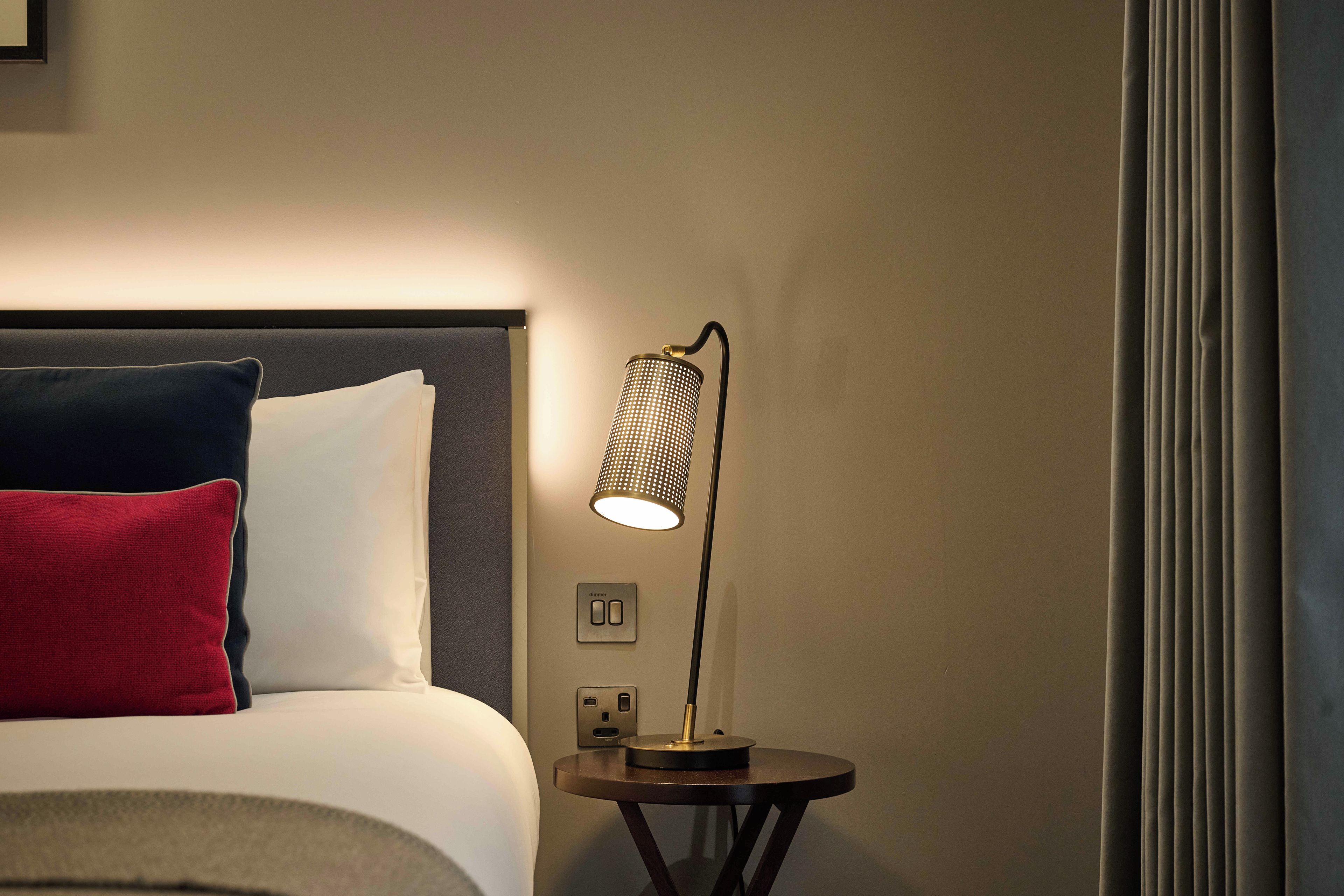 A bed with a headboard, a bedside lamp, and a power outlet on the wall.