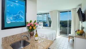 A hotel room with a kitchen area, a bed, a balcony with a view, and a mounted TV. - Rare Unobstructed Diamond Head-Ocean Views, Best location, Pool, 1 minute to Beach (Honolulu)
