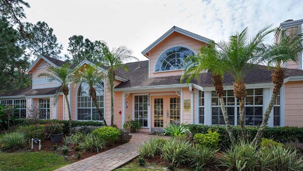 A two-story building with a central entrance, surrounded by palm trees and a brick pathway. - Royal Palm Villa (Kissimmee)