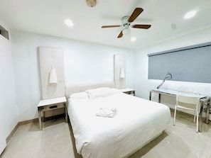 A hotel room with a bed, desk, chair, ceiling fan, and two wall-mounted lamps.
