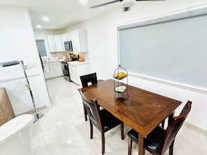 A dining area with a wooden table and chairs, a white refrigerator, a microwave, and a window with a view.
