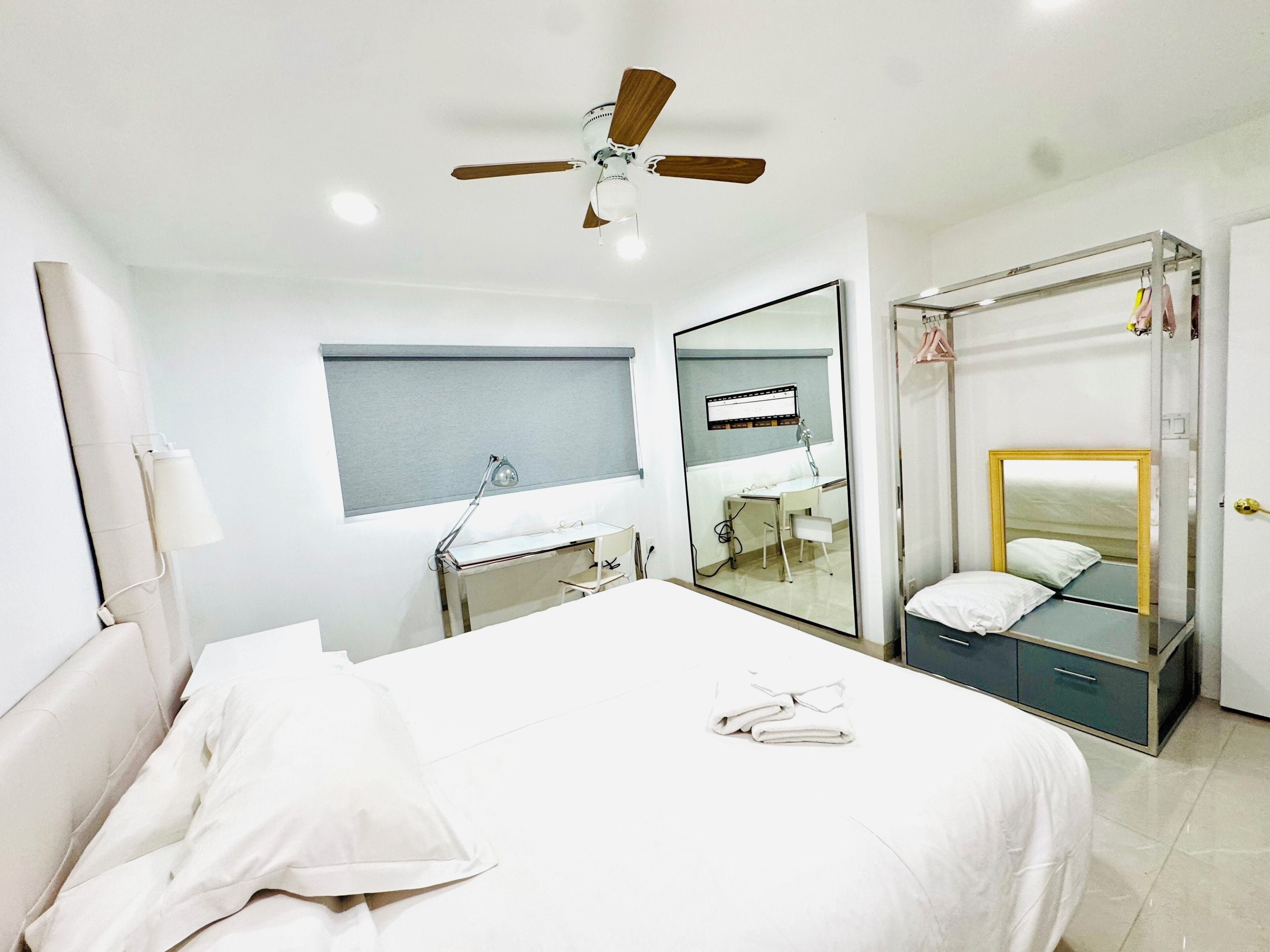 Ein Hotelzimmer mit Bett, Schreibtisch, Stuhl, Spiegel, Deckenventilator und Kleiderschrank.