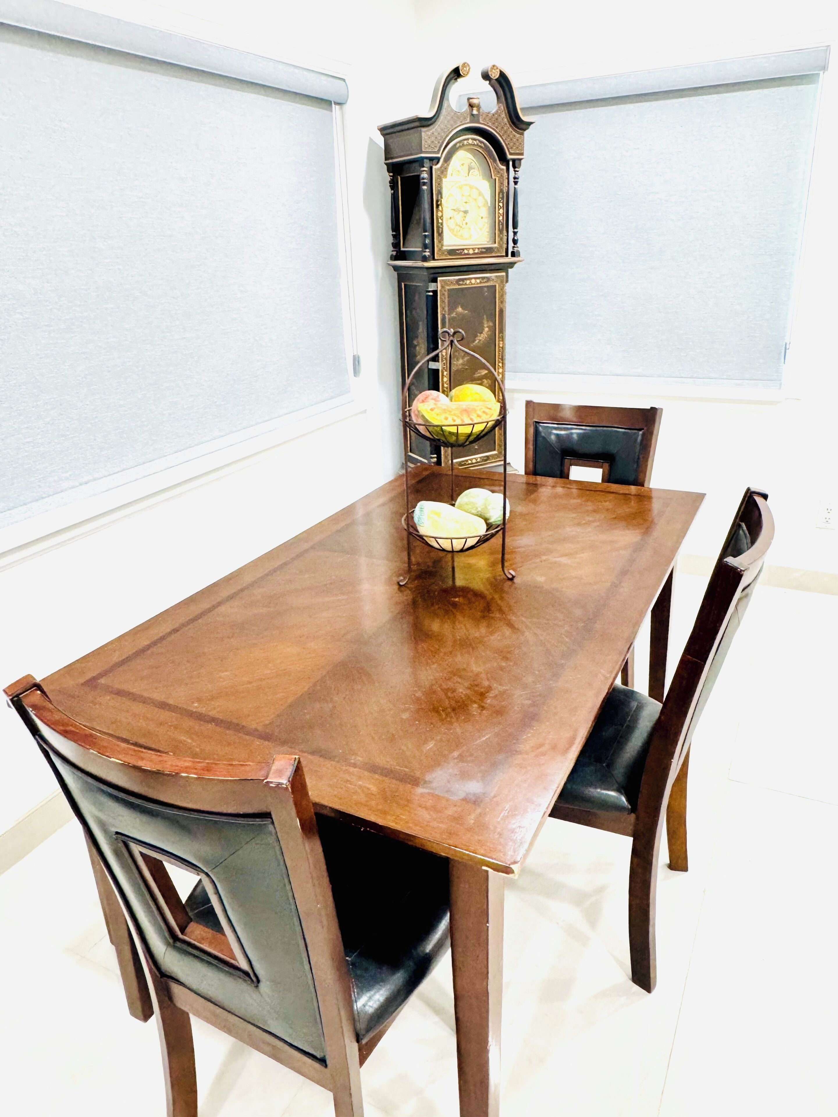 Una mesa de comedor con sillas, un reloj en la pared y una cesta de frutas.