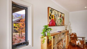 Una habitación con chimenea, una ventana con vistas a hojas otoñales y un cuadro en la pared.