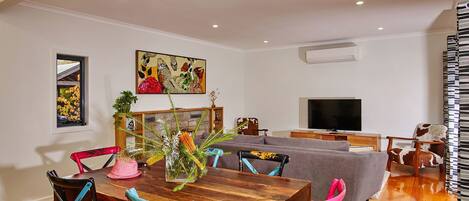 Un comedor con una mesa de madera, sillas coloridas, una chimenea y un televisor en un salón moderno.