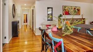 Un comedor con una mesa de madera, sillas coloridas y un cuadro en la pared.