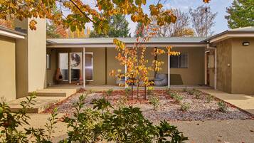 A building with a covered patio area, outdoor seating, and a small tree with autumn leaves.