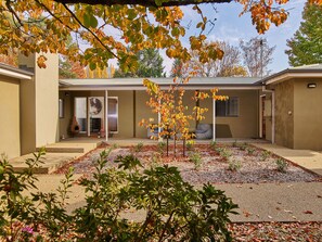 A building with a covered patio area, outdoor seating, and a small tree with autumn leaves. - Northbank House (Bright)