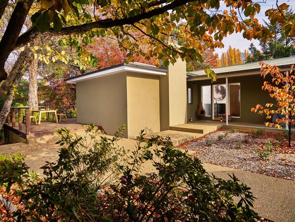 A modern house with a patio area, a fireplace, and a garden with autumn foliage. - Northbank House (Bright)