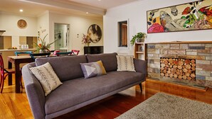 Una sala de estar con sofá gris, piso de madera, chimenea con le ña y un comedor con sillas y mesa.