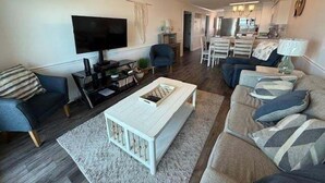 Ein modernes Wohnzimmer mit einem Flachbildfernseher, einem Deckenventilator und einem Essbereich mit weißen Stühlen.