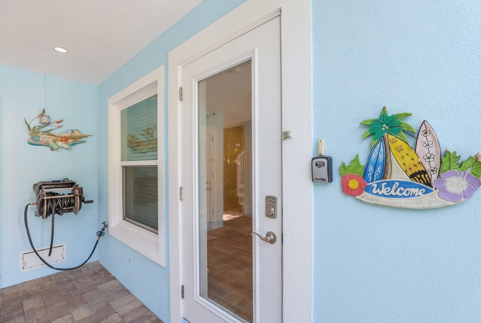 A hallway with a door leading to a room, a wall-mounted security device, and a welcome sign with tropical decorations.