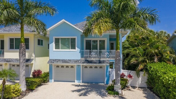 Une maison à deux étages avec une façade bleue et jaune, un balcon et une allée menant à un garage.
