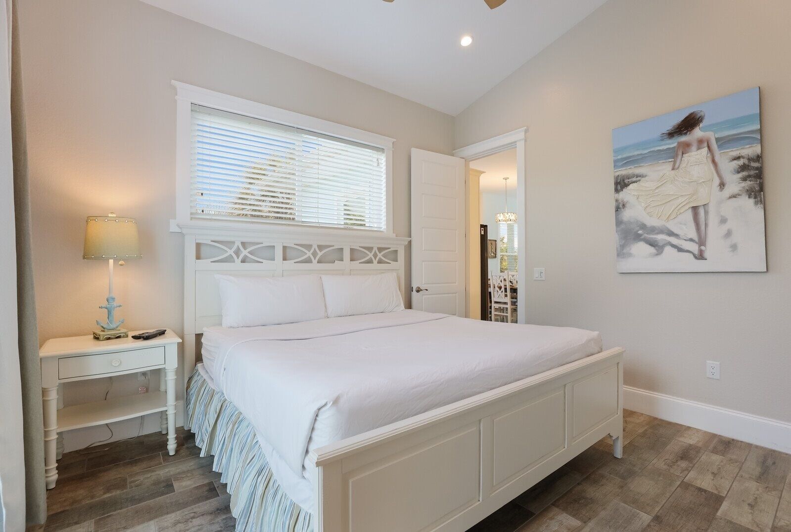 Un dormitorio con cama, mesita de noche, lámpara y un cuadro en la pared.