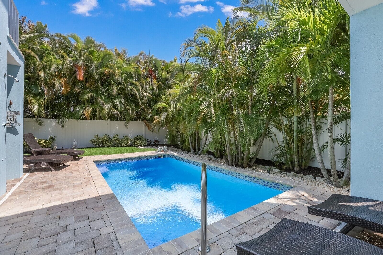 A swimming pool with lounge chairs, surrounded by palm trees and a white wall.