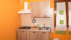Una cocina con armarios de madera, una estufa a gas, un lavamanos y un cubo de basura.