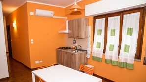 Una cocina compacta con una mesa blanca y sillas naranjas, una encimera pequeña y una ventana con cortinas.