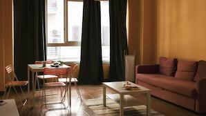 Ein Wohnzimmer mit einer Couch, einem Esstisch mit Stühlen, einem Couchtisch und einem Fenster mit Vorhängen.
