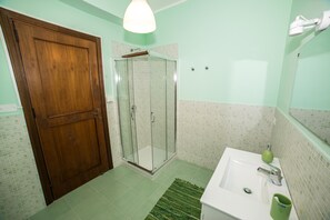 A bathroom with a wooden door, a glass shower enclosure, a sink with a green soap dispenser, and a mirror. - Loft Notarbartolo 2 (Palermo)
