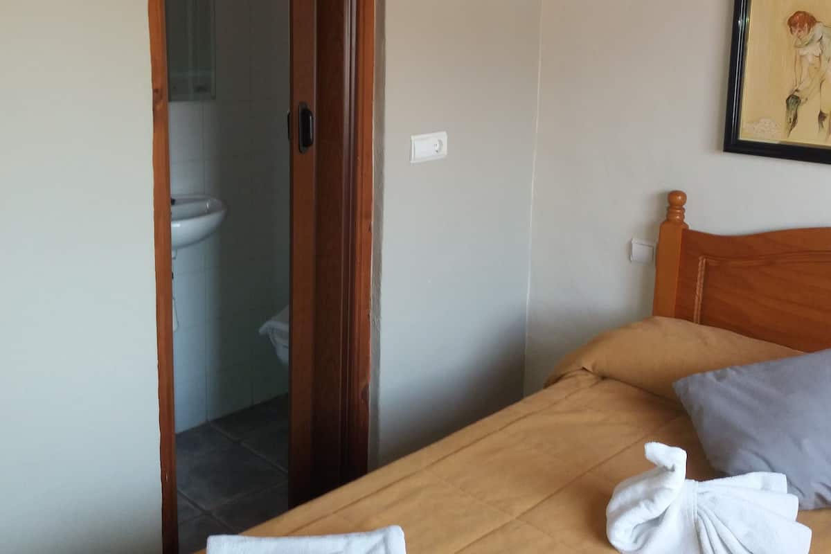 A bedroom with a wooden bed, a wooden headboard, a framed picture on the wall, and a bathroom visible through an open door.