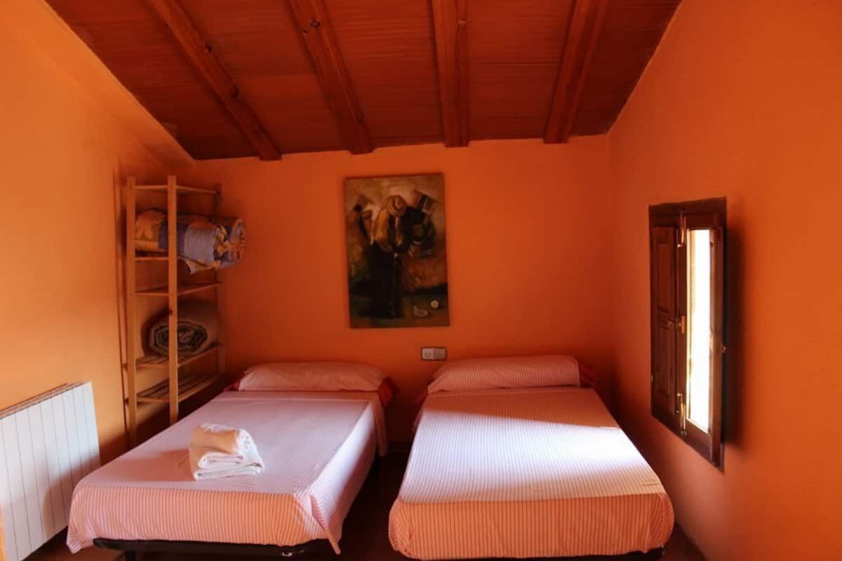 A room with two beds, a wooden shelf unit, a painting on the wall, and a window.