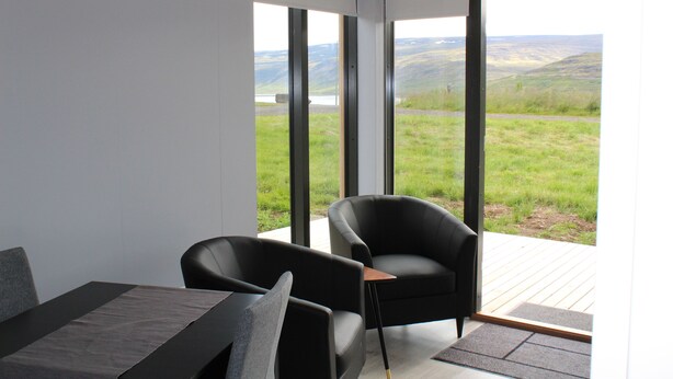 A modern room with a large window, a black chair, and a dining table. - Systrakot (Talknafjordur)