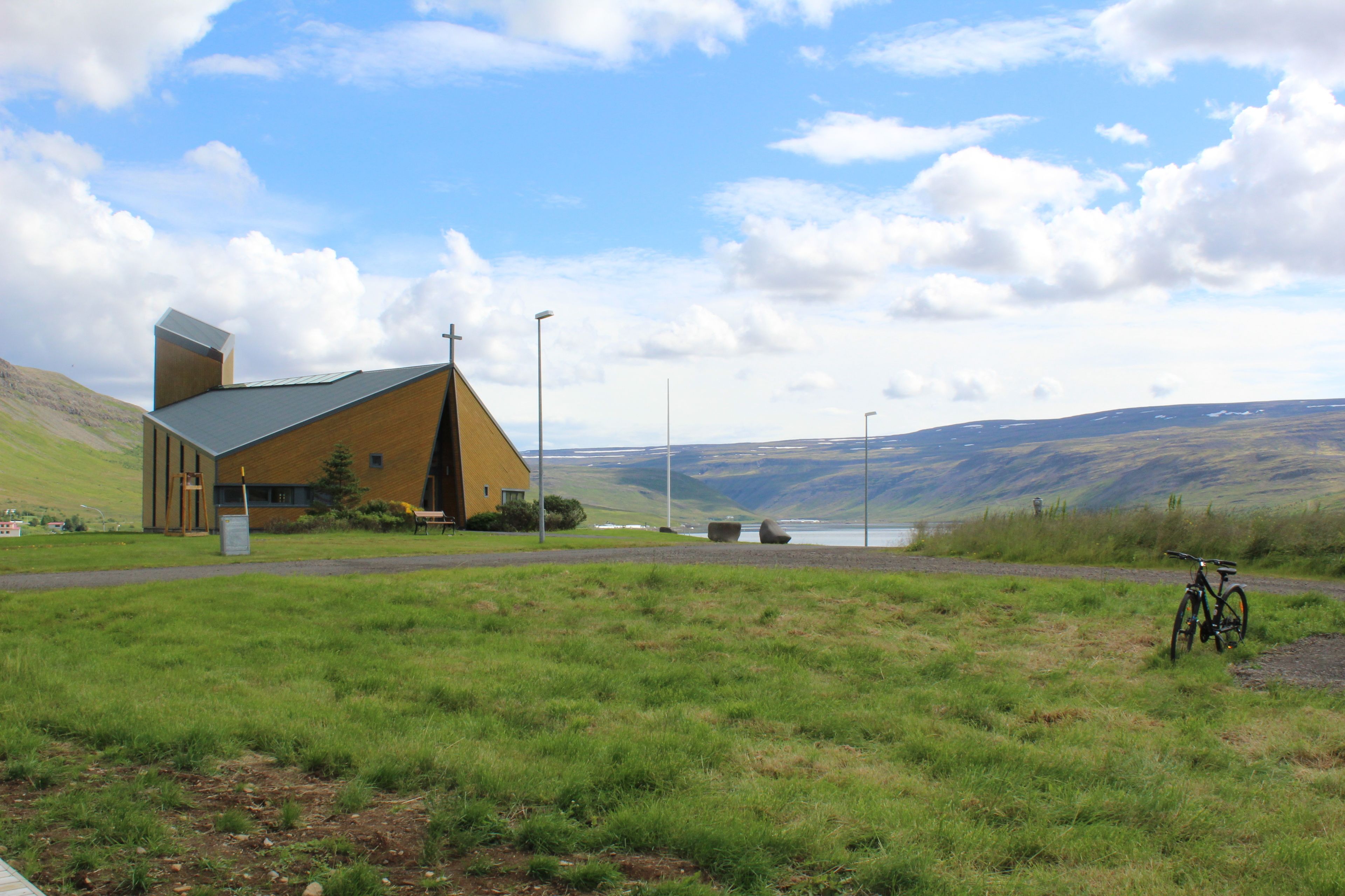 A building with a sloped roof and a cross on the front, set against a backdrop of hills and a clear sky.