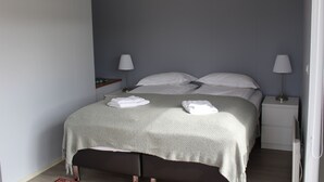 A neatly made bed with pillows and a blanket, two bedside lamps, a small bedside table, and a nightstand with a lamp. - Systrakot (Talknafjordur)
