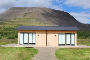 Edificio moderno con fachada de madera y grandes puertas de cristal, ubicado en una zona verde con una montaña al fondo.