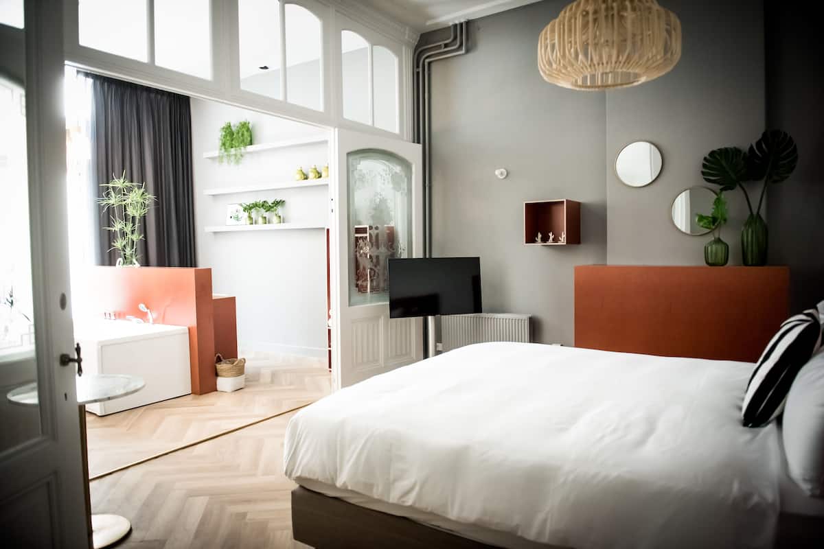 A modern bedroom with a large bed, a television, and a bathroom with a sink and mirror.
