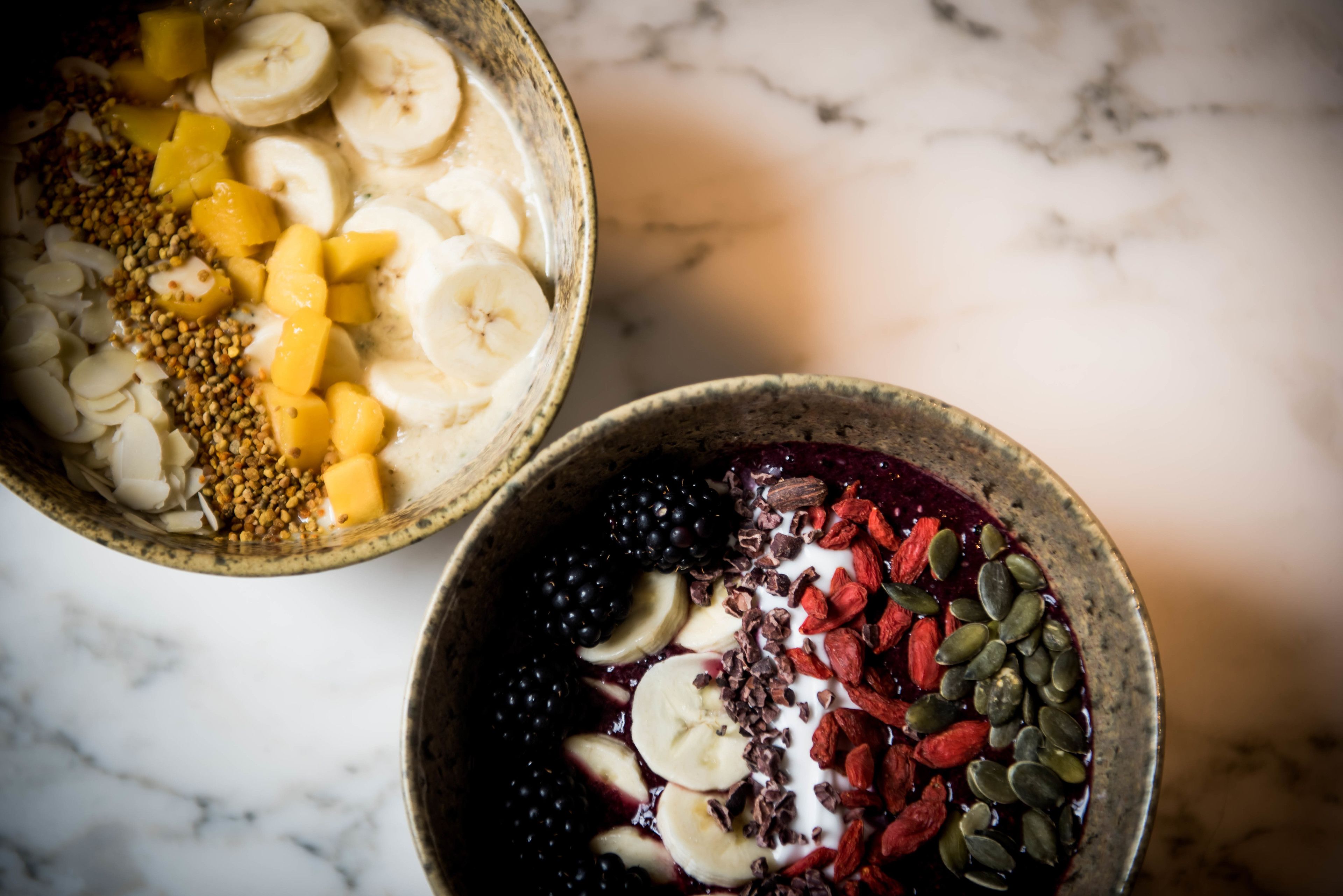 Deux bols de fruits et de granola sur une surface en marbre.