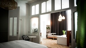 Une chambre d’hôtel moderne avec un grand lit, une petite table ronde, un canapé et une vue sur le salon attenant.