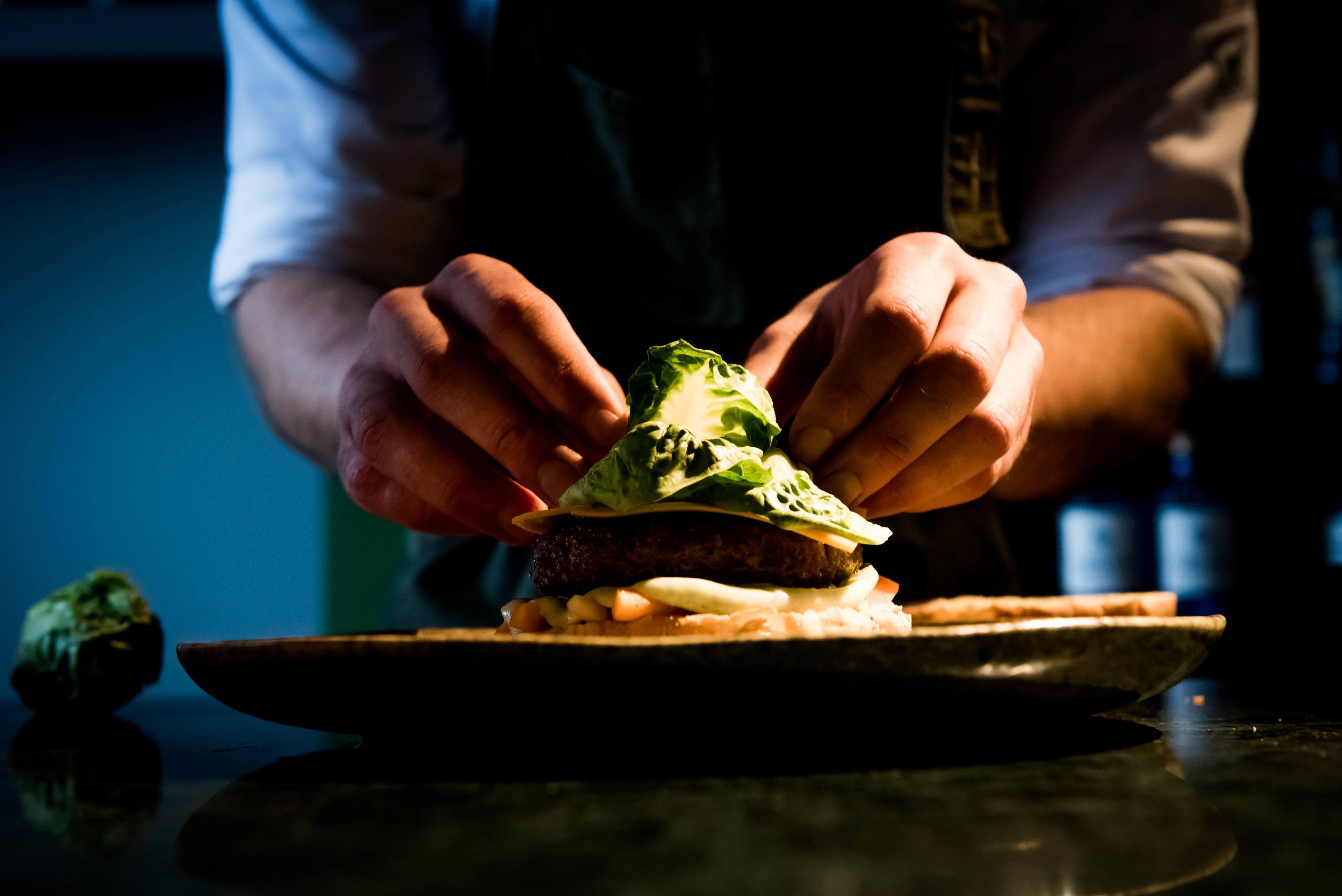 A person assembling a burger with lettuce and cheese on a plate.
