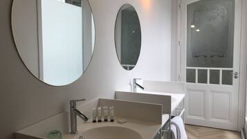 A modern bathroom with a large oval mirror, a rectangular sink, and a frosted glass door.