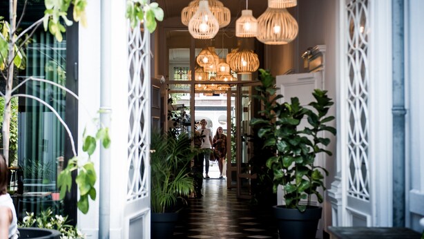 Un couloir agrémenté de lampes en osier suspendues, de plantes en pot et d’une rambarde décorative blanche.