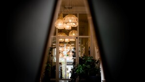Une vue à travers l'encadrement d'une porte, donnant sur une pièce où pendent de nombreuses lampes en osier et où sont disposées des plantes en pot.