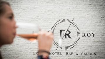 Ein Logo mit den Buchstaben "TR" und "ROY" auf einer strukturierten Wand, und der Text "UR HOTEL, BAR & GARDEN" darunter.