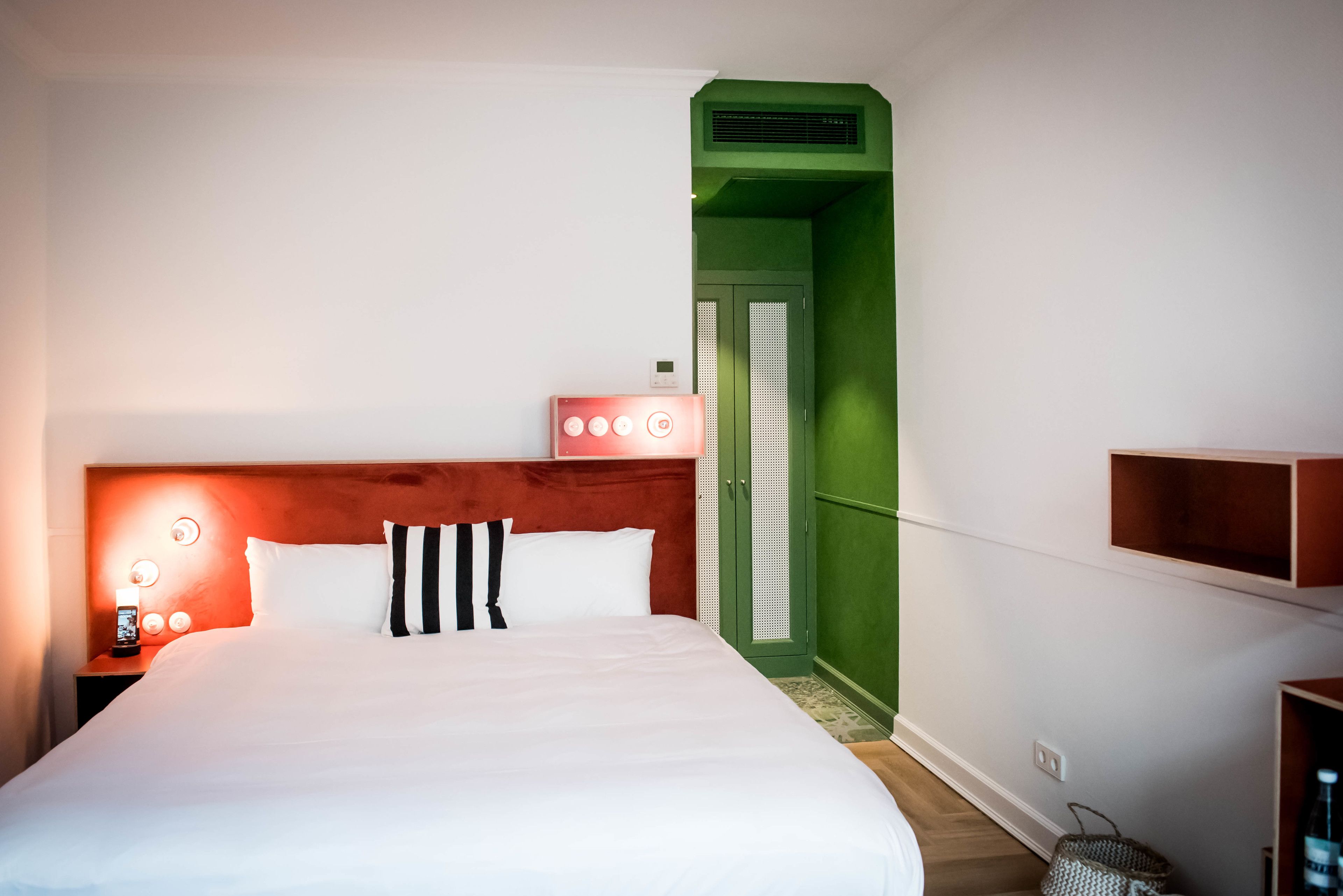 Hotelkamer met een groot bed, een houten hoofdbord, een nachtkastje met een lamp en een groene deur naar een badkamer.