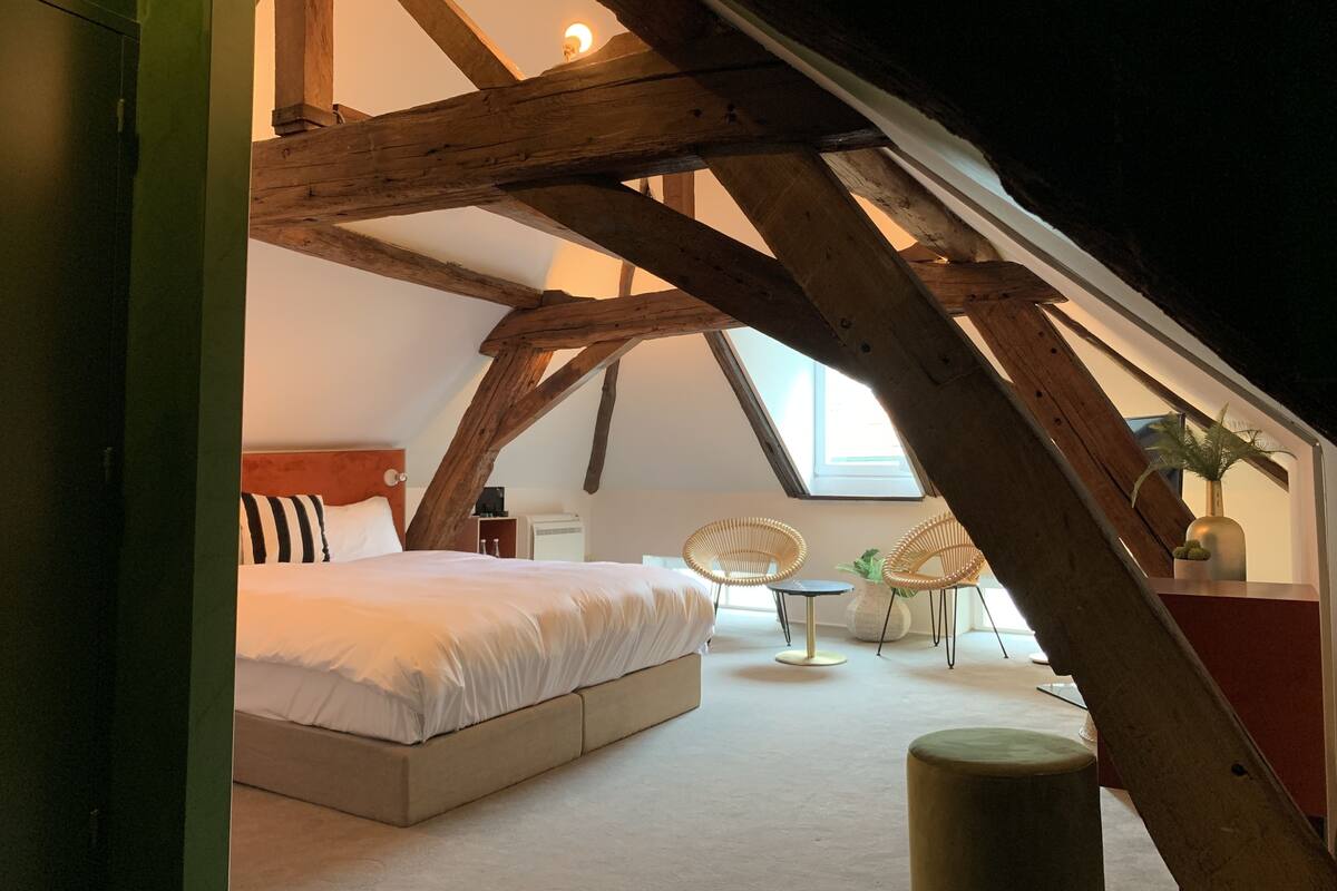 A bedroom with a sloped ceiling, a bed, a small table, two chairs, and a window.