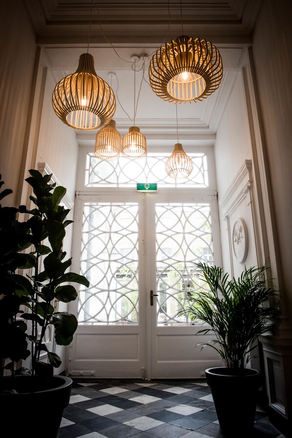 A hallway with a checkered floor, a white door with a geometric glass pattern, and three hanging wicker lamps.