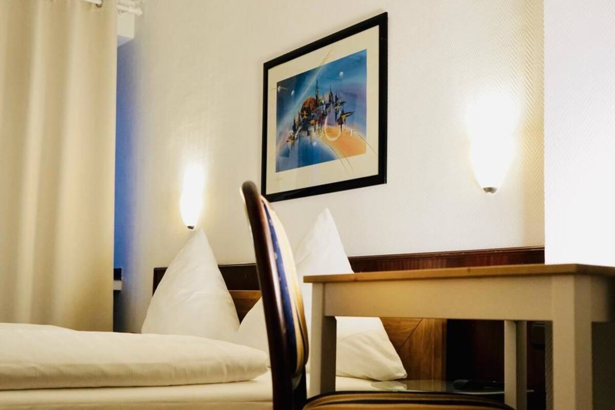 Hotellihuone, jossa on sänky, tuoli, pöytä ja seinällä oleva kehystetty kuva.