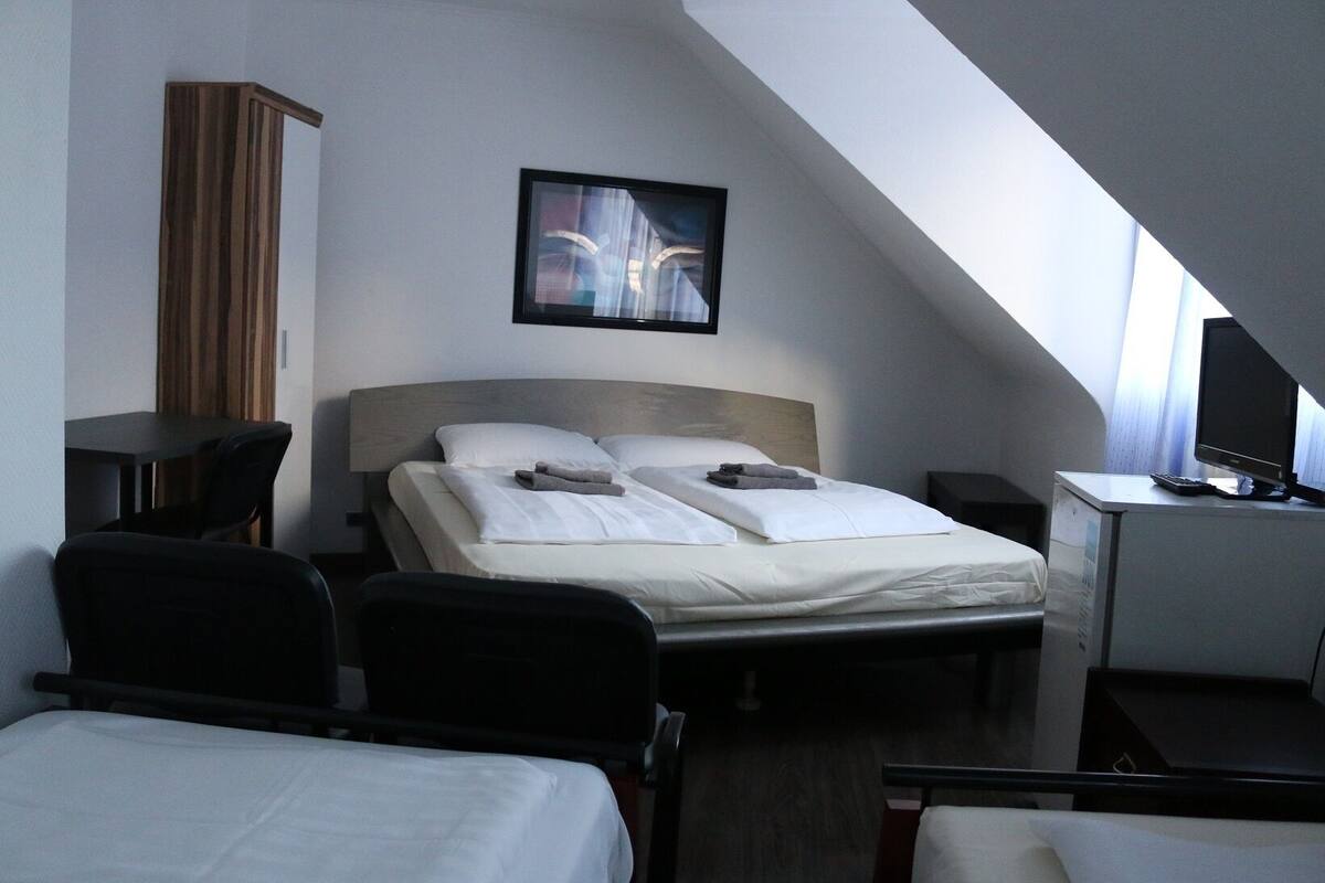 Hotellihuone, jossa on sänky, kaksi yöpöytää, työpöytä tietokoneella ja tuoli.