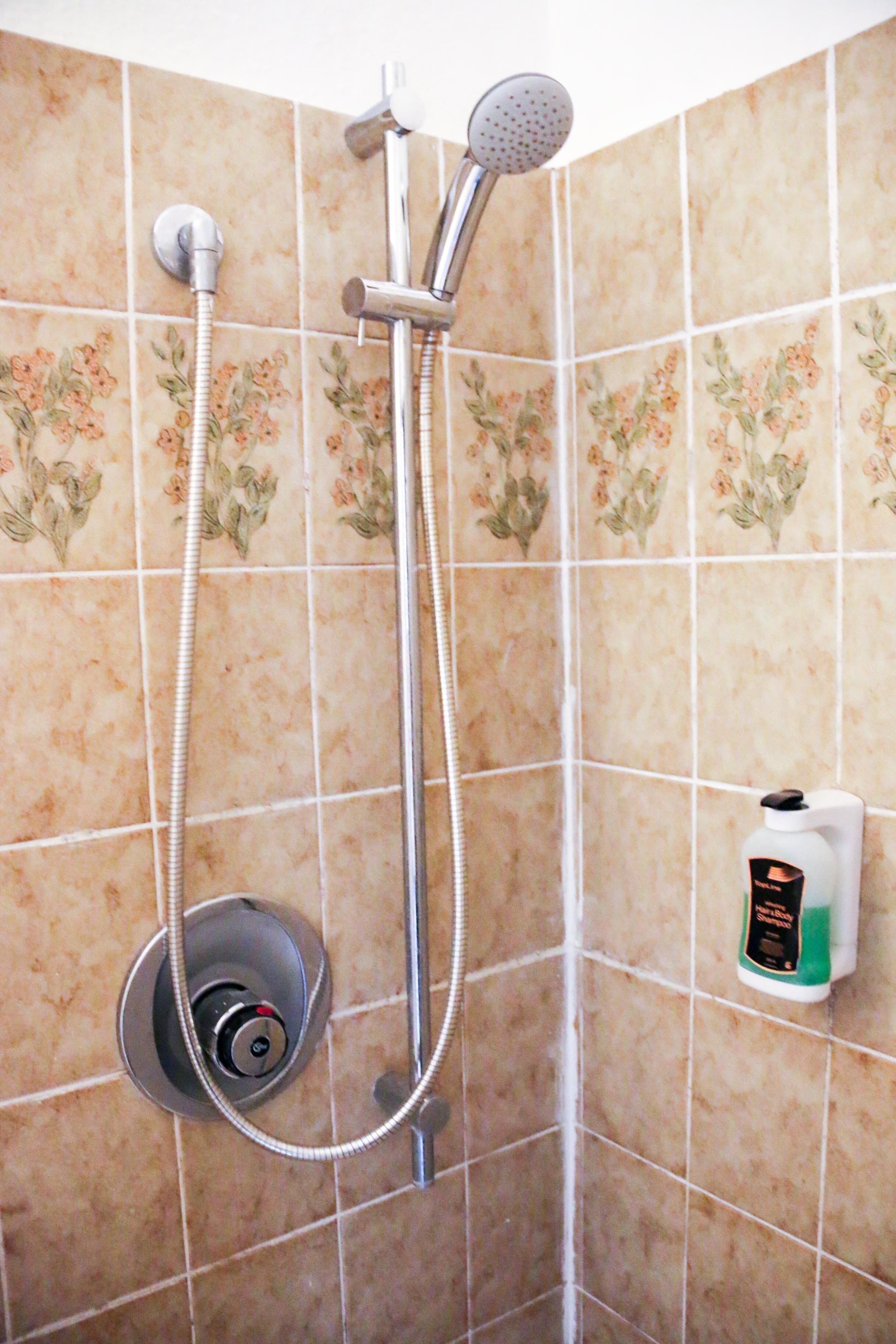 Una ducha con cabezal de ducha manual y panel de control en la pared.