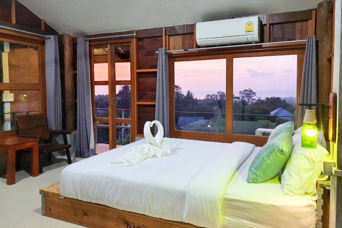A bedroom with a wooden bed, a desk, and a large window with a view.