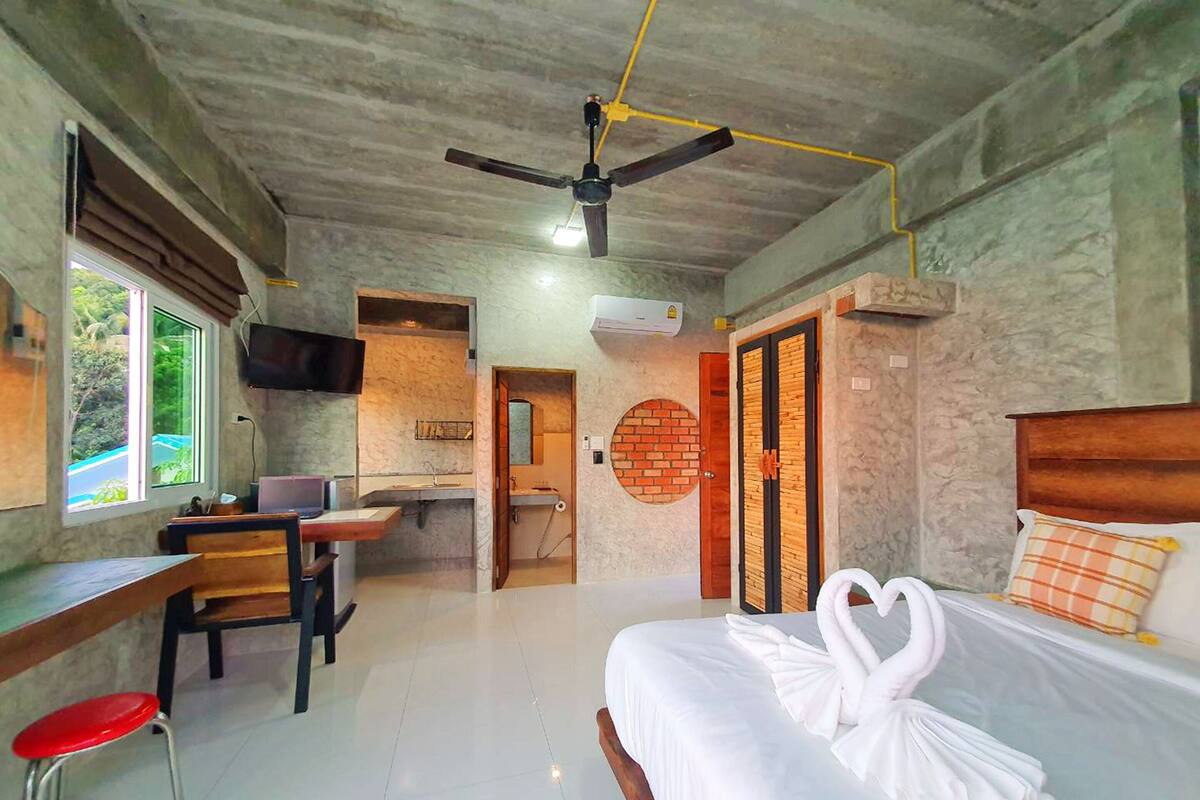 A bedroom with a bed, a desk, a chair, a ceiling fan, and a bathroom.