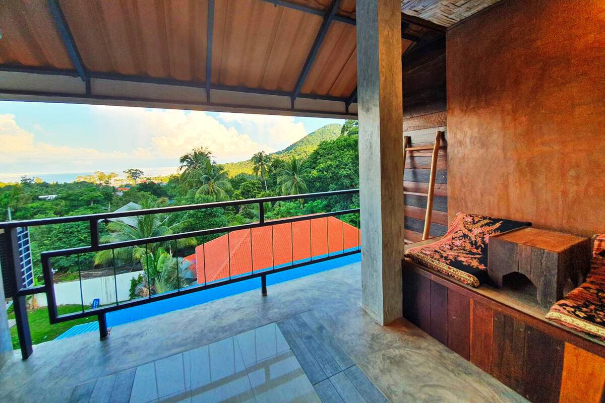 A balcony with a view of lush greenery and a distant coastline.