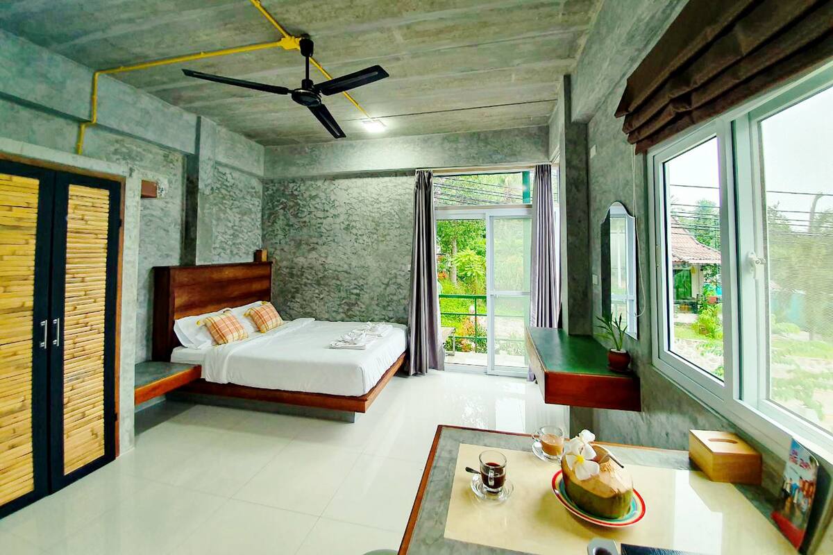 A bedroom with a bed, a ceiling fan, a window with curtains, and a view of greenery outside.