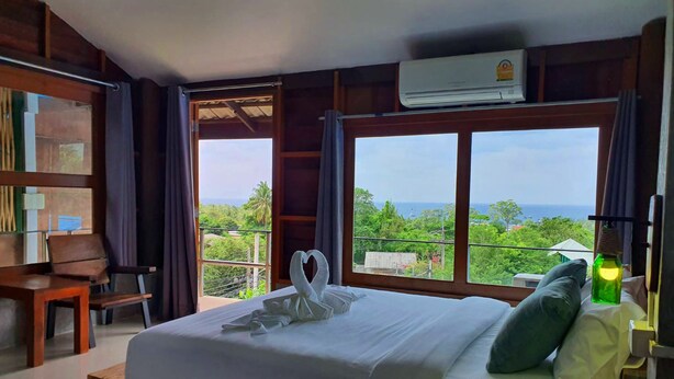 Ein Schlafzimmer mit einem Bett, einer Holzbank, einer grünen Flasche und Blick auf den Ozean.