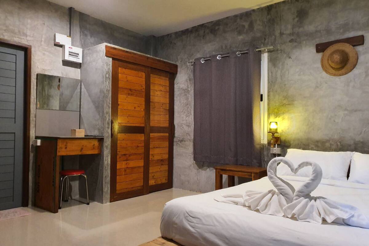 A bedroom with a bed, a wooden wardrobe, a desk with a chair, a mirror, and a wall-mounted hat.