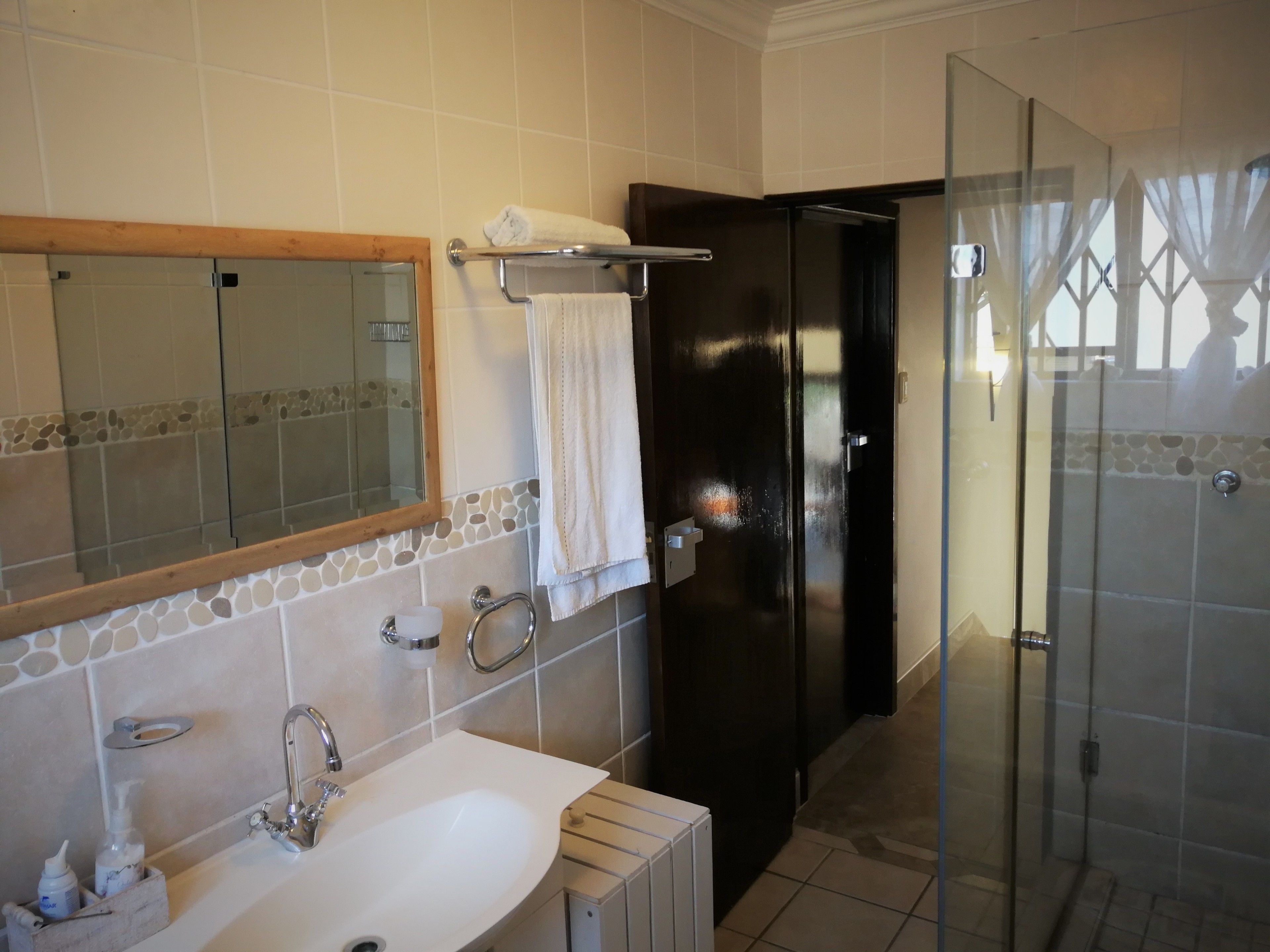 A bathroom with a white sink, a mirror, a towel rack, and a glass shower enclosure.